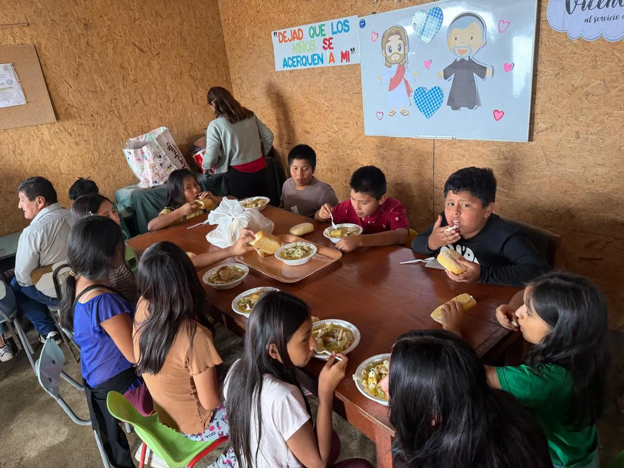 Niños comiendo sopa en mesas junto al cartel "Dejad que los niños se acerquen a mí"